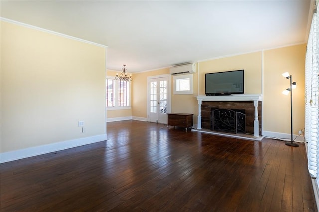 unfurnished living room featuring crown molding, a notable chandelier, a fireplace with raised hearth, a wall unit AC, and dark wood-type flooring