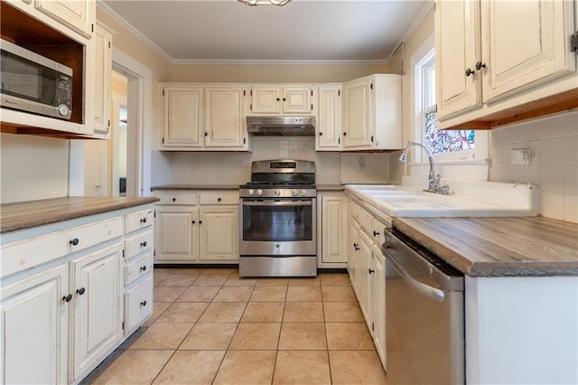 kitchen with light tile patterned flooring, under cabinet range hood, a sink, backsplash, and stainless steel appliances