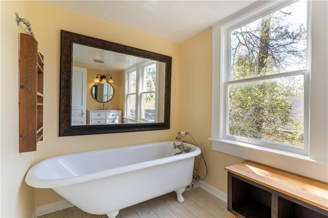 bathroom with baseboards, plenty of natural light, a soaking tub, and vanity