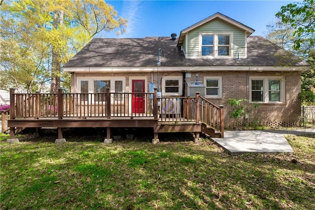rear view of property with a deck, a patio, brick siding, a shingled roof, and a lawn