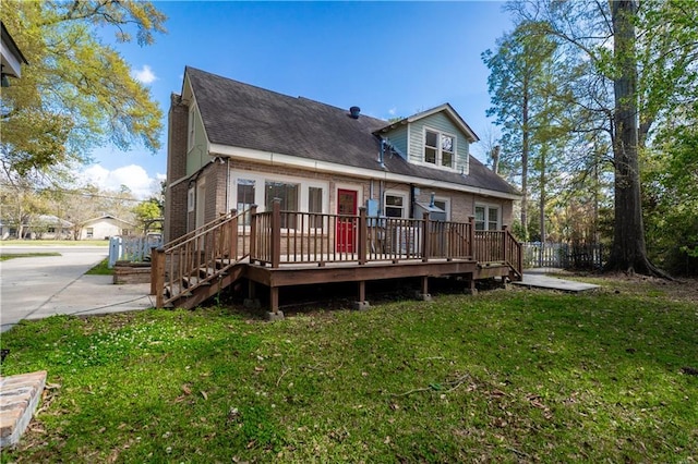 back of house with a lawn, a deck, brick siding, and roof with shingles