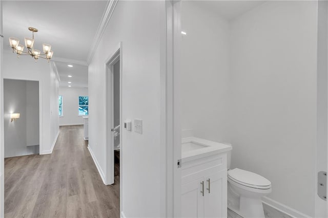 bathroom with an inviting chandelier, toilet, baseboards, wood finished floors, and ornamental molding