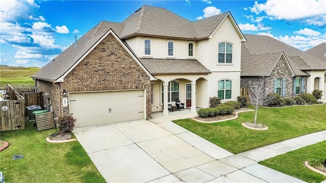 french country inspired facade with fence, a front yard, stucco siding, a garage, and driveway