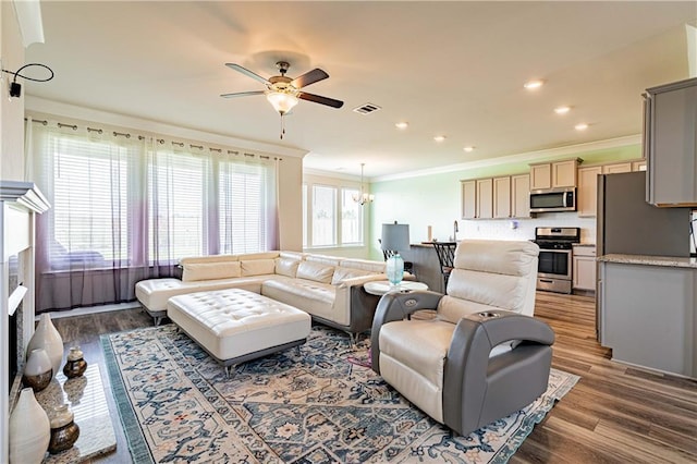 living room with recessed lighting, wood finished floors, ornamental molding, and ceiling fan with notable chandelier