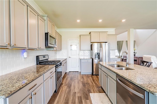 kitchen with light stone counters, wood finished floors, a sink, stainless steel appliances, and tasteful backsplash