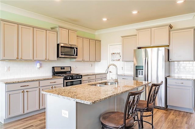 kitchen featuring light wood finished floors, an island with sink, a sink, stainless steel appliances, and a kitchen bar
