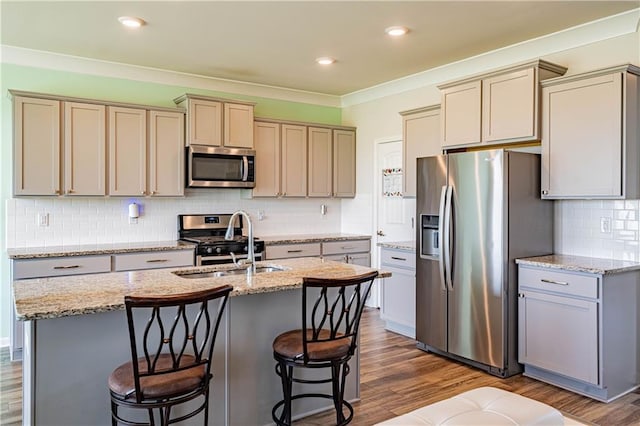 kitchen with a center island with sink, a sink, dark wood-type flooring, appliances with stainless steel finishes, and crown molding