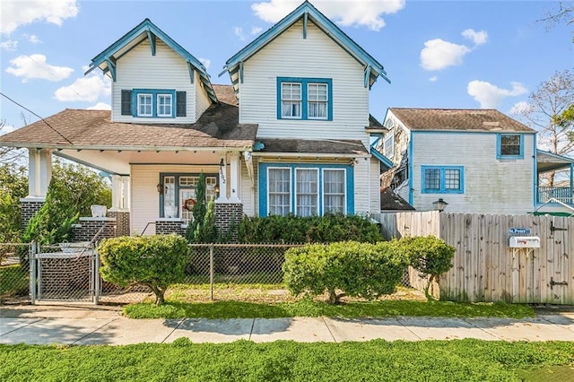 view of front facade featuring a fenced front yard, a porch, a shingled roof, and a gate