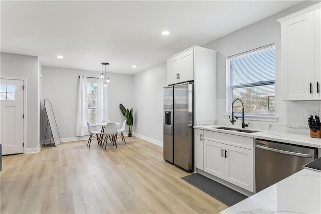 kitchen with light stone countertops, light wood-type flooring, white cabinets, a sink, and stainless steel appliances