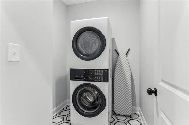 clothes washing area with stacked washing maching and dryer, laundry area, and baseboards