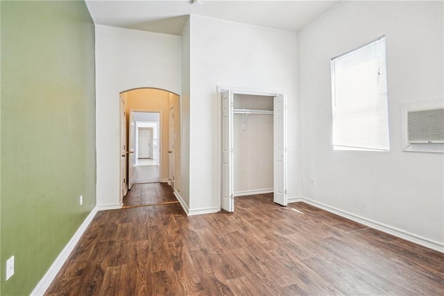 320709 Bienville St, New Orleans, LA 70119 - unfurnished bedroom with a wall mounted AC, a closet, baseboards, dark wood-type flooring, and arched walkways