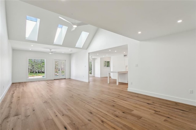 unfurnished living room with a skylight, high vaulted ceiling, light wood-style flooring, baseboards, and recessed lighting