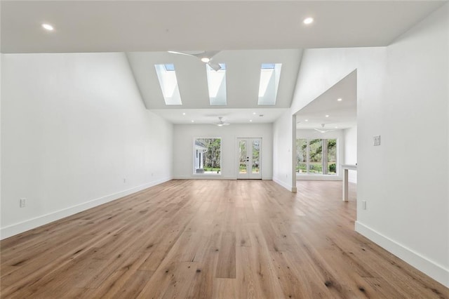 unfurnished living room featuring a skylight, light wood-type flooring, baseboards, high vaulted ceiling, and recessed lighting