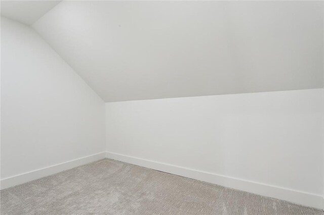 bonus room with vaulted ceiling, light colored carpet, and baseboards