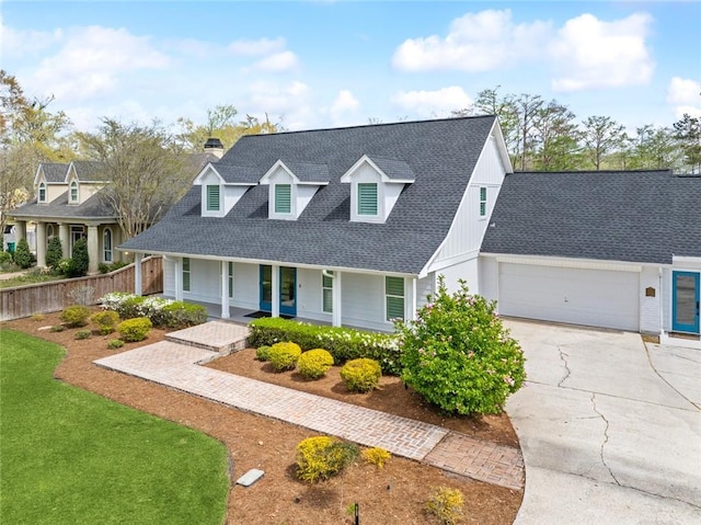 cape cod house with concrete driveway, a shingled roof, a porch, a chimney, and an attached garage