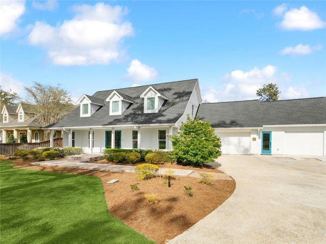 new england style home featuring concrete driveway, a porch, an attached garage, a front yard, and a shingled roof