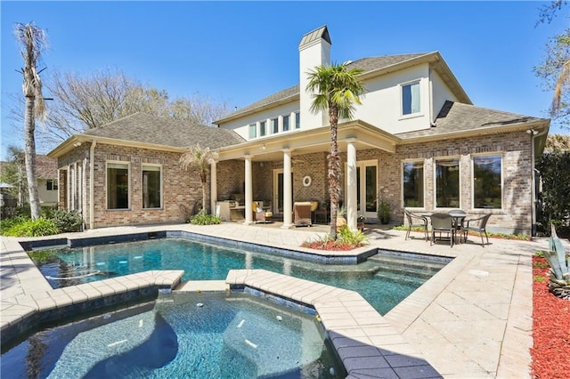192 Forest Oaks Dr, New Orleans, LA 70131 - rear view of house featuring a patio area, a pool with connected hot tub, a chimney, and brick siding