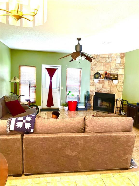 living room featuring a stone fireplace, a textured ceiling, and a ceiling fan