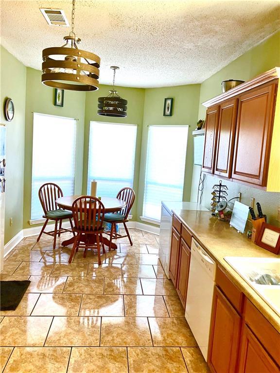 kitchen with visible vents, a textured ceiling, white dishwasher, light countertops, and hanging light fixtures