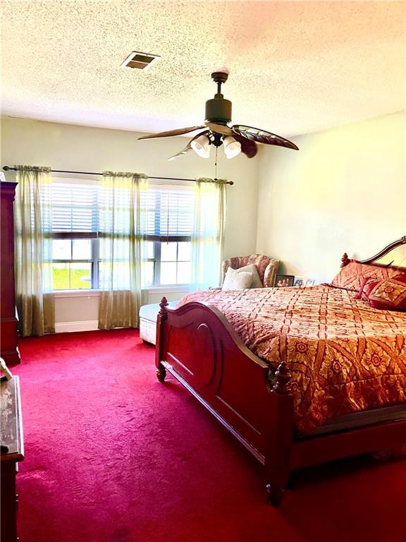carpeted bedroom with visible vents, a textured ceiling, and ceiling fan