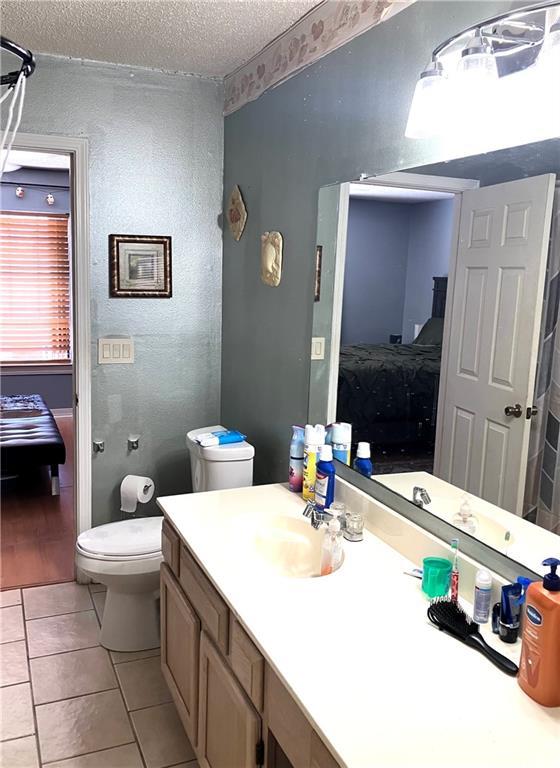ensuite bathroom with toilet, ensuite bathroom, a textured ceiling, tile patterned flooring, and vanity