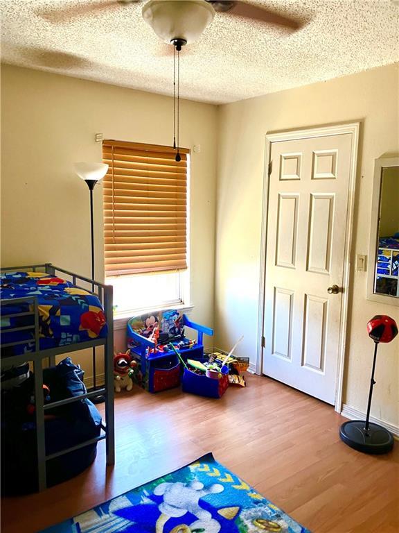 playroom with baseboards, a textured ceiling, wood finished floors, and a ceiling fan