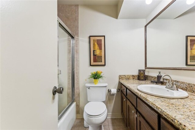 bathroom featuring baseboards, toilet, tile patterned floors, vanity, and enclosed tub / shower combo
