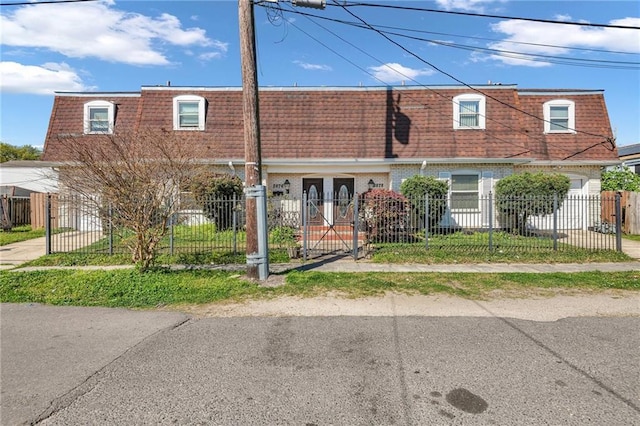 multi unit property featuring brick siding, a fenced front yard, and mansard roof