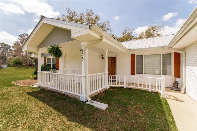 view of side of property with a lawn, metal roof, covered porch, and brick siding
