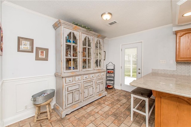 kitchen featuring tasteful backsplash, a breakfast bar area, glass insert cabinets, and crown molding