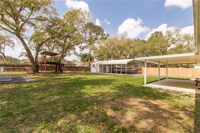 view of yard featuring a detached carport, a fenced backyard, and a playground