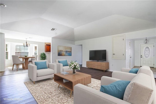 living area with a notable chandelier, visible vents, wood finished floors, and vaulted ceiling