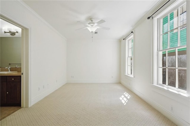 empty room with ceiling fan, light colored carpet, crown molding, a sink, and baseboards