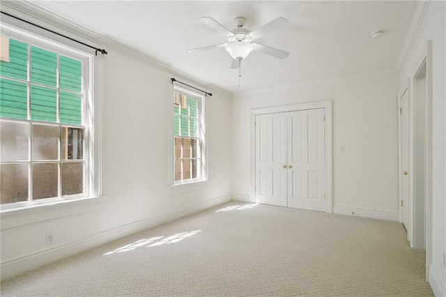 unfurnished bedroom featuring carpet, ornamental molding, a closet, baseboards, and a ceiling fan