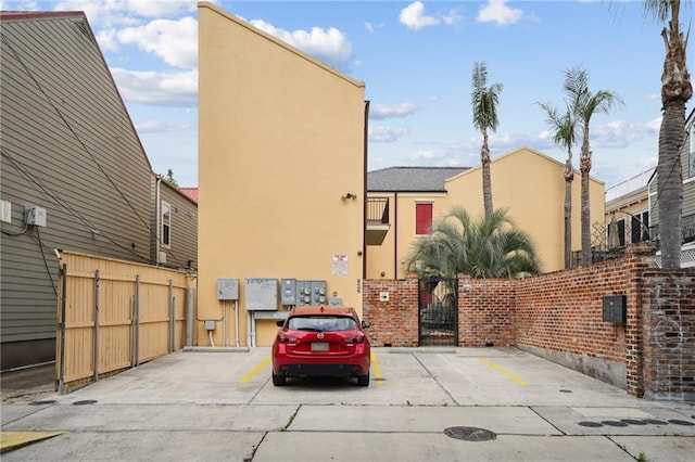 view of front of home with stucco siding, uncovered parking, fence, and a gate