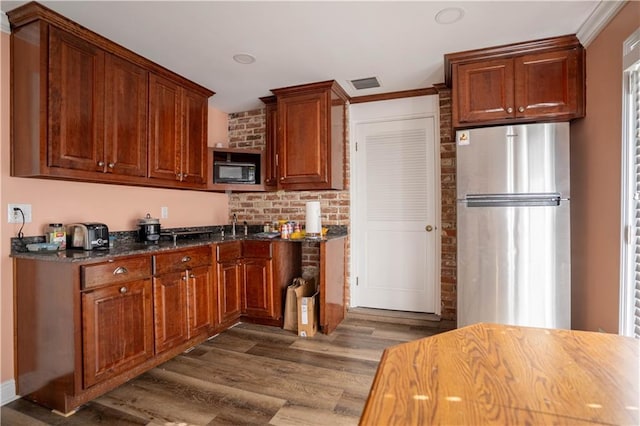 4012 Berot St, Metairie, LA 70002 - kitchen with freestanding refrigerator, black microwave, dark wood-style floors, ornamental molding, and dark stone counters