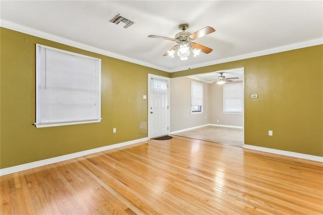 spare room with crown molding, light wood-type flooring, baseboards, ceiling fan, and visible vents