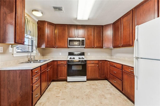 kitchen with visible vents, stainless steel microwave, a sink, gas range, and freestanding refrigerator