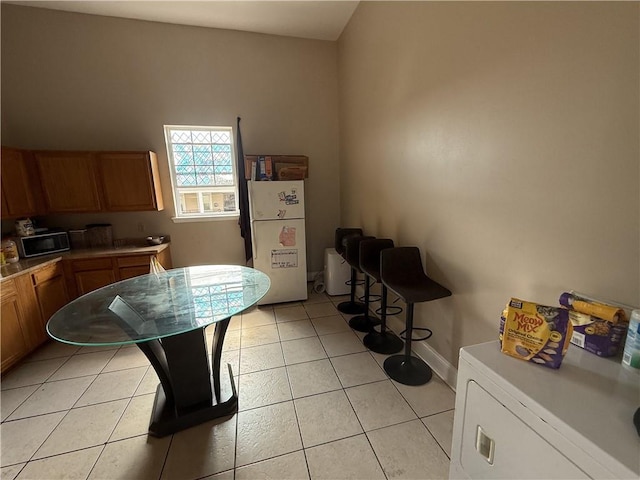 1827 S Rampart St, New Orleans, LA 70113 - kitchen featuring freestanding refrigerator, brown cabinetry, washer / clothes dryer, light tile patterned flooring, and baseboards