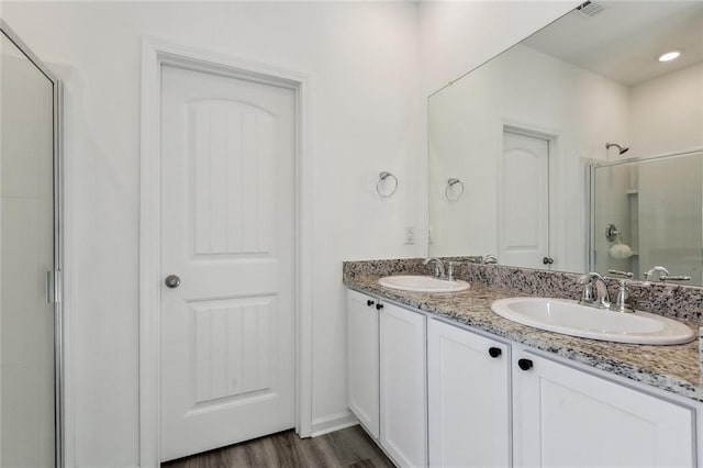 bathroom featuring a shower stall, wood finished floors, double vanity, and a sink
