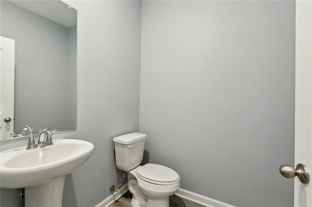 bathroom featuring toilet, baseboards, wood finished floors, and a sink