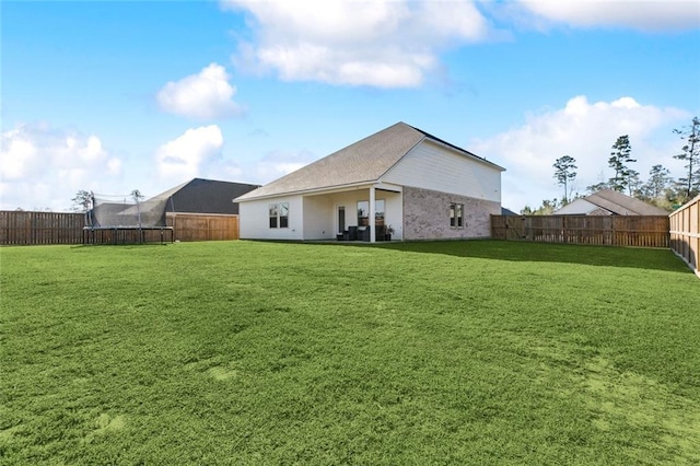 rear view of house with a yard, a fenced backyard, and a trampoline