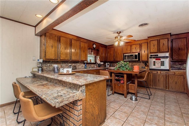59345 Twin Pines Rd, Bogalusa, LA 70427 - kitchen featuring a peninsula, appliances with stainless steel finishes, brown cabinetry, and visible vents