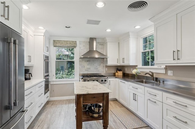 1338 Fern St, New Orleans, LA 70118 - kitchen featuring appliances with stainless steel finishes, wall chimney exhaust hood, a sink, white cabinets, and light wood-type flooring