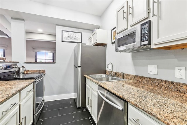 kitchen featuring dark tile patterned floors, appliances with stainless steel finishes, a sink, baseboards, and light stone counters