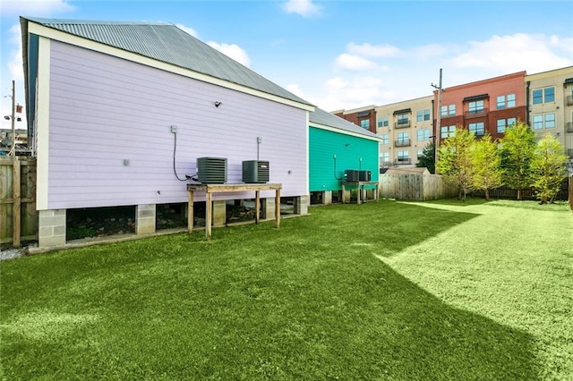 rear view of house featuring metal roof, central AC, fence, and a lawn