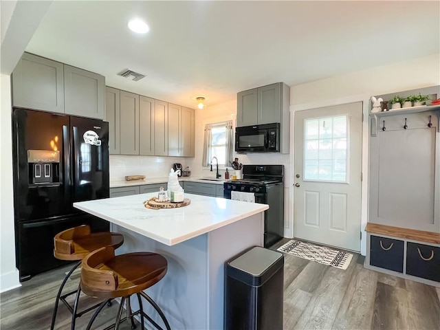 kitchen with gray cabinets, a sink, a breakfast bar area, visible vents, and black appliances
