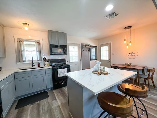 kitchen featuring a sink, wood finished floors, a kitchen breakfast bar, visible vents, and black appliances