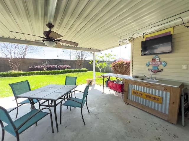 view of patio with fence, a sink, outdoor dining space, and a ceiling fan