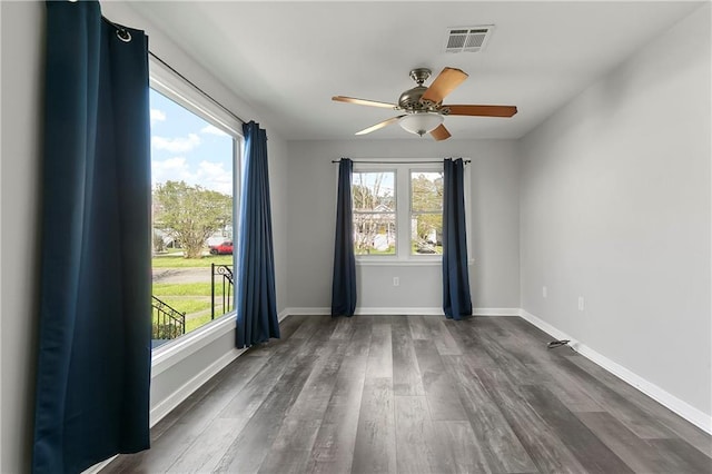 empty room with dark wood-style flooring, ceiling fan, visible vents, and plenty of natural light